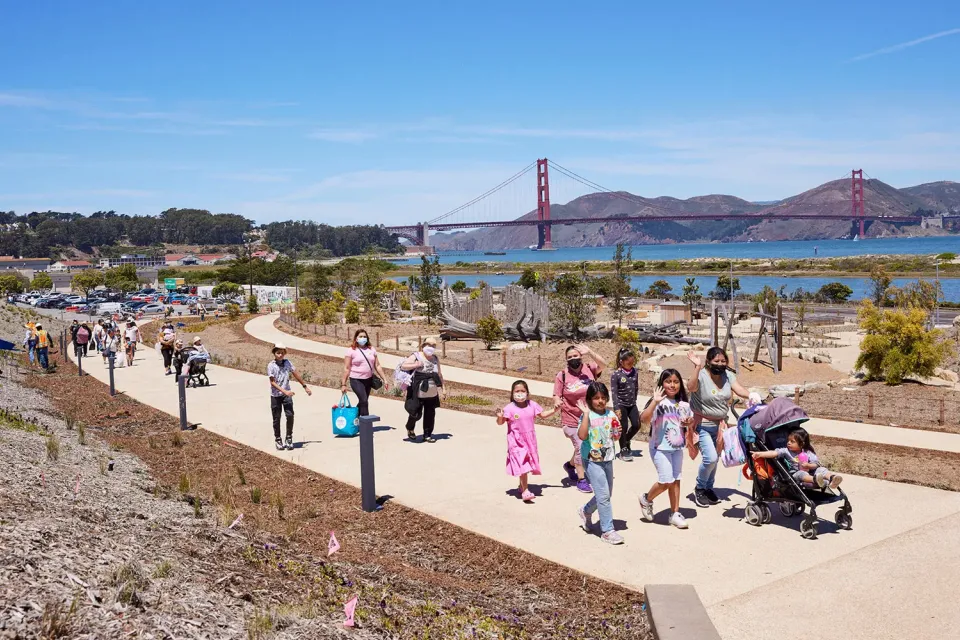 People walking on a concrete pathway at Presidio Tunnel Tops with the Golden Gate Bridge in the background